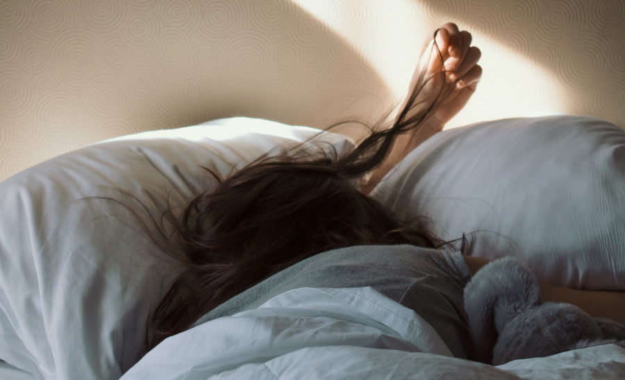 Γυναίκα στο κρεβάτι σκεπασμένη με πάπλωμα ακουμπάει τα μαλιά της